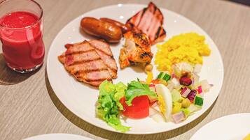Un plato de comida con carne a la parrilla, salchichas y una ensalada de verduras variadas.