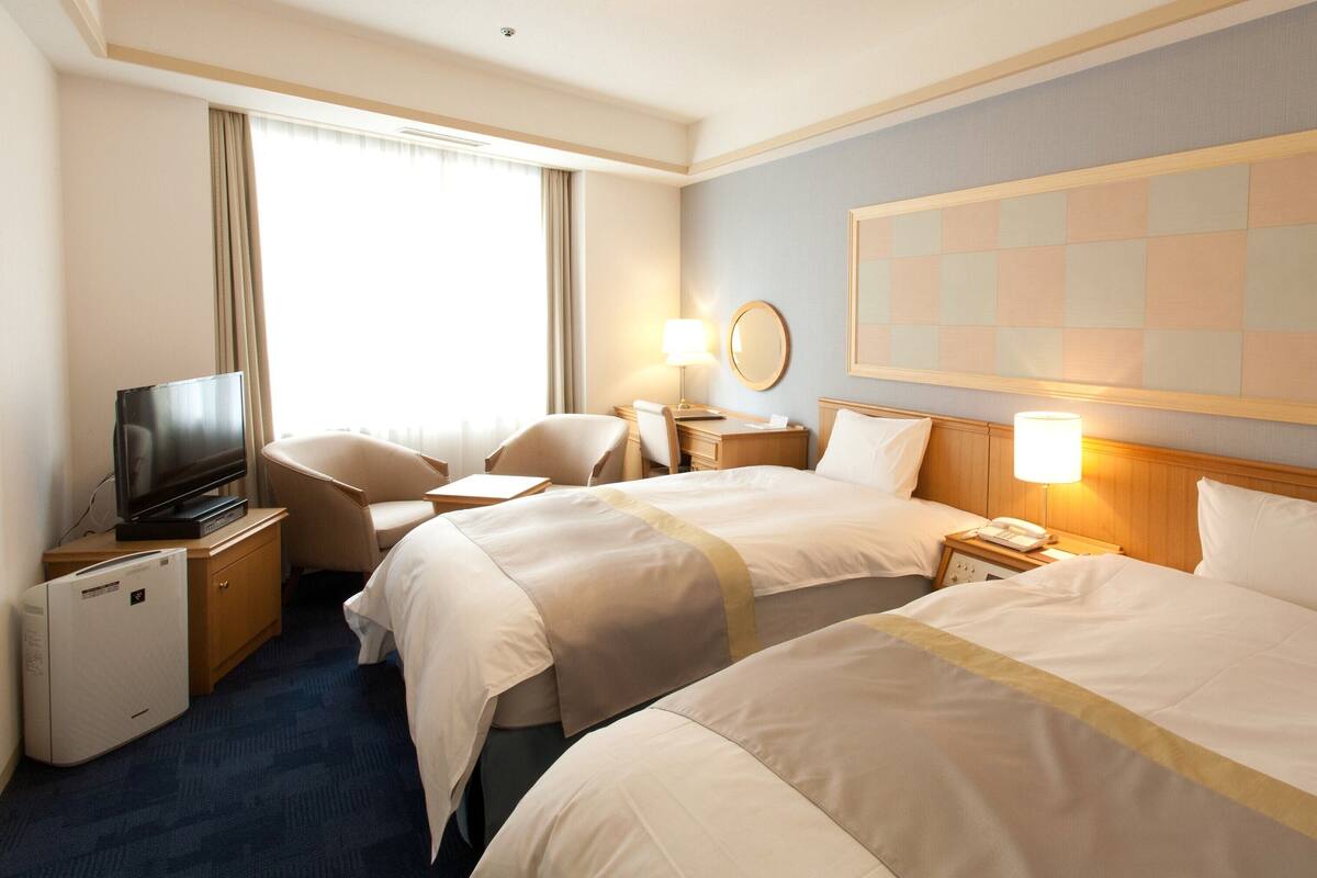 A hotel room with two beds, a television, a desk, and a chair.