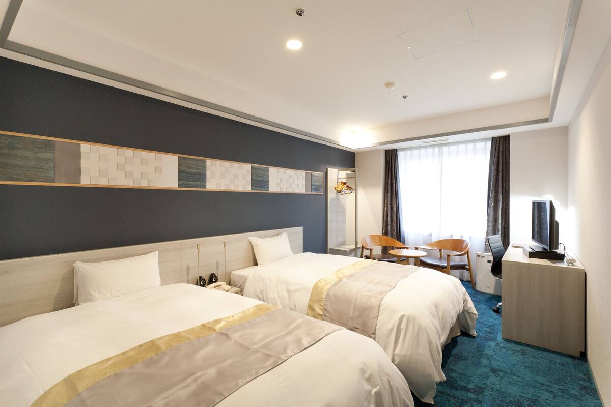 A hotel room with two beds, a desk with a computer, a chair, and a TV.