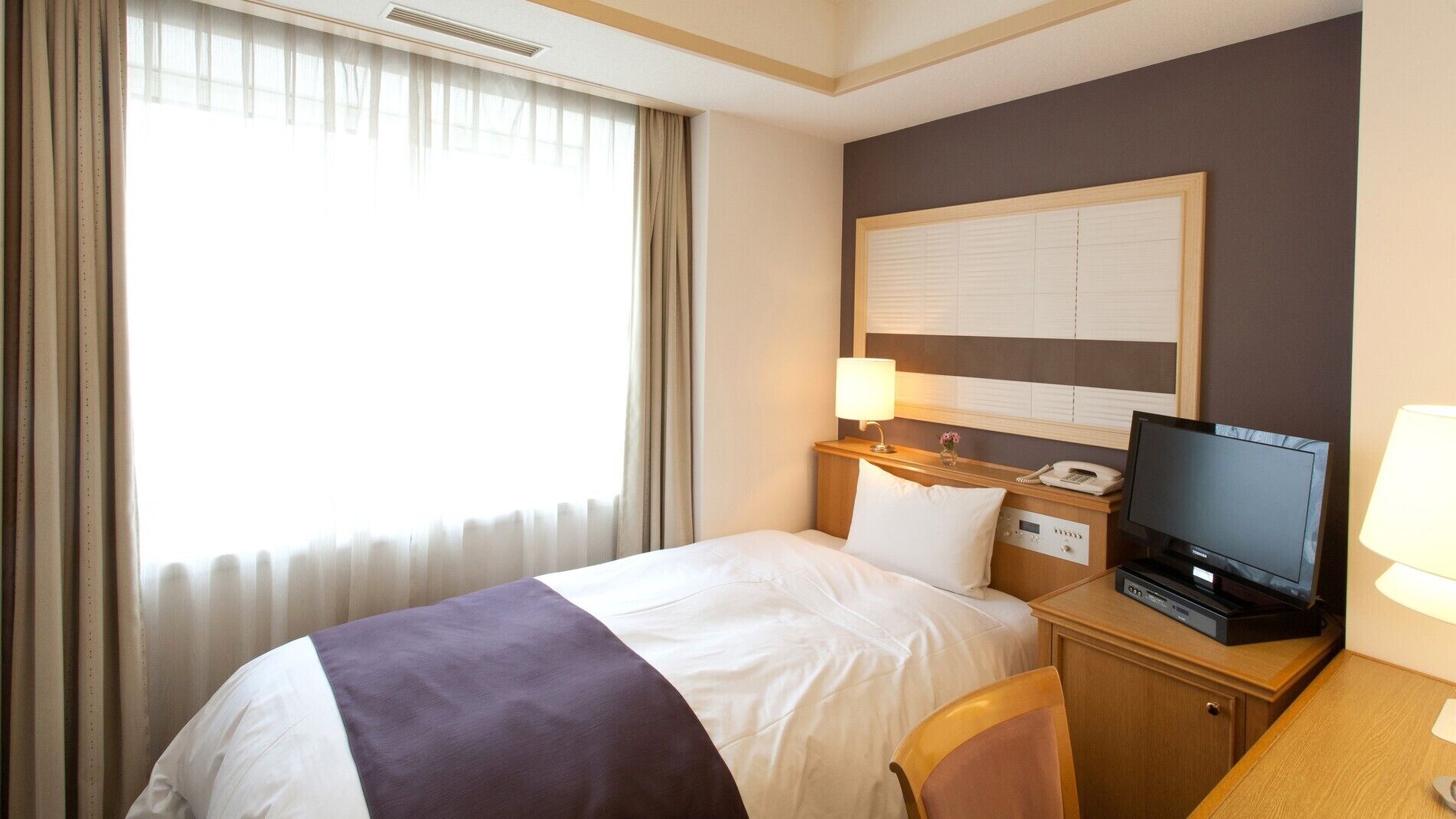 Une chambre d’hôtel comprenant un lit, un bureau avec une télévision, un téléphone et une lampe.