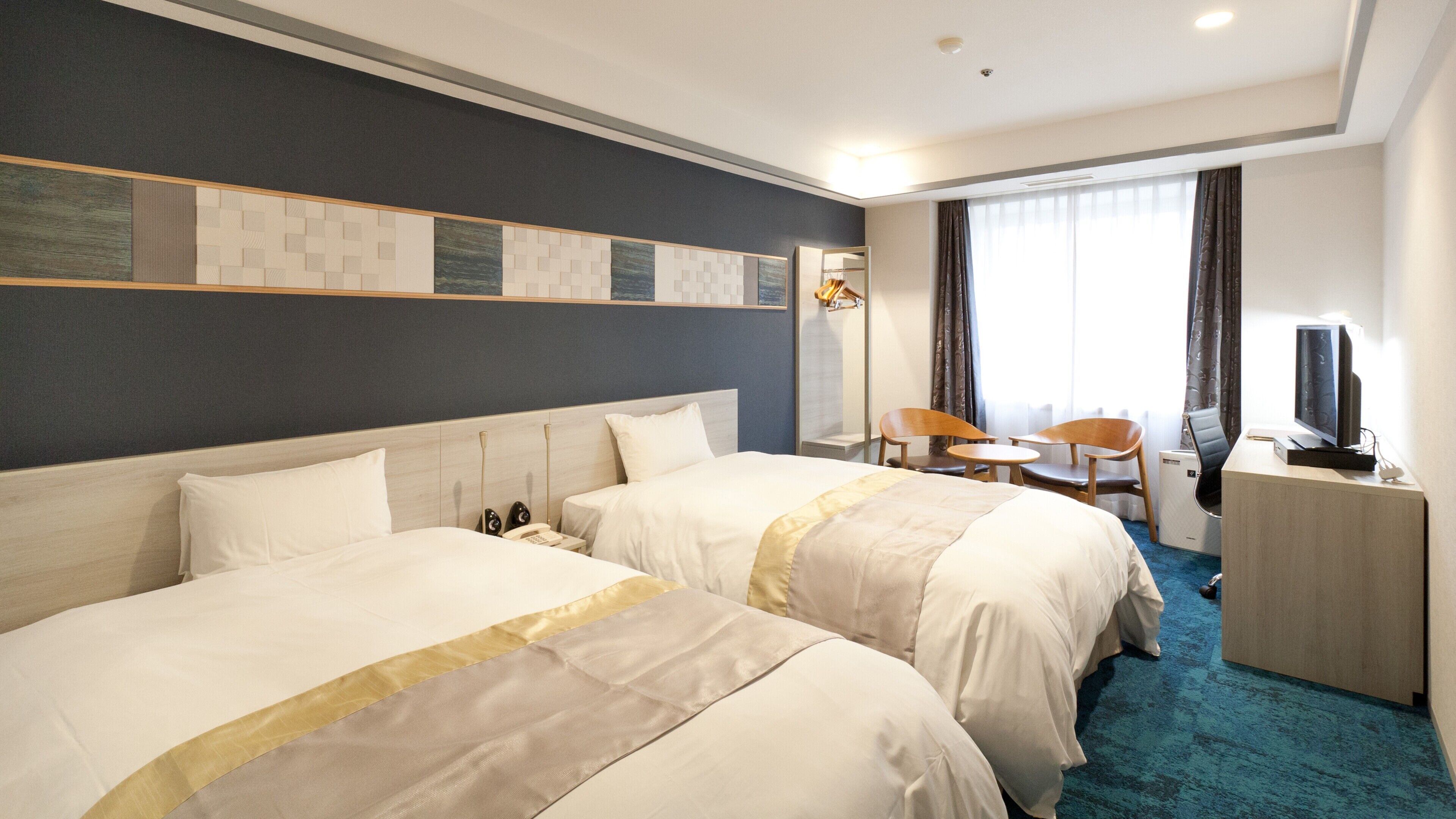 A hotel room with two beds, a desk with a TV, a chair, and a small table.
