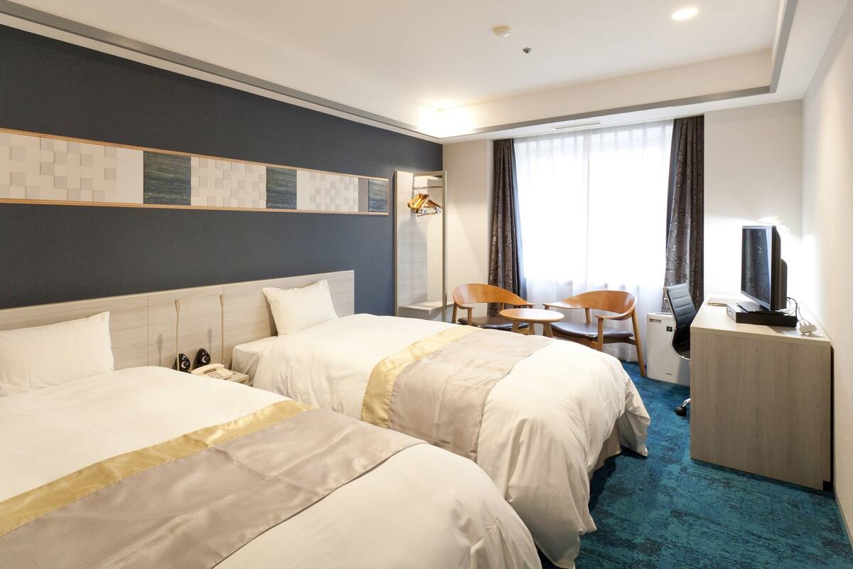 A hotel room with two beds, a desk with a TV, a chair, and a small table.