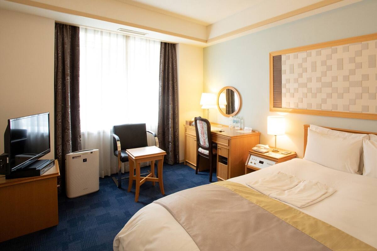 A hotel room with a bed, desk, chair, television, and a window with curtains.