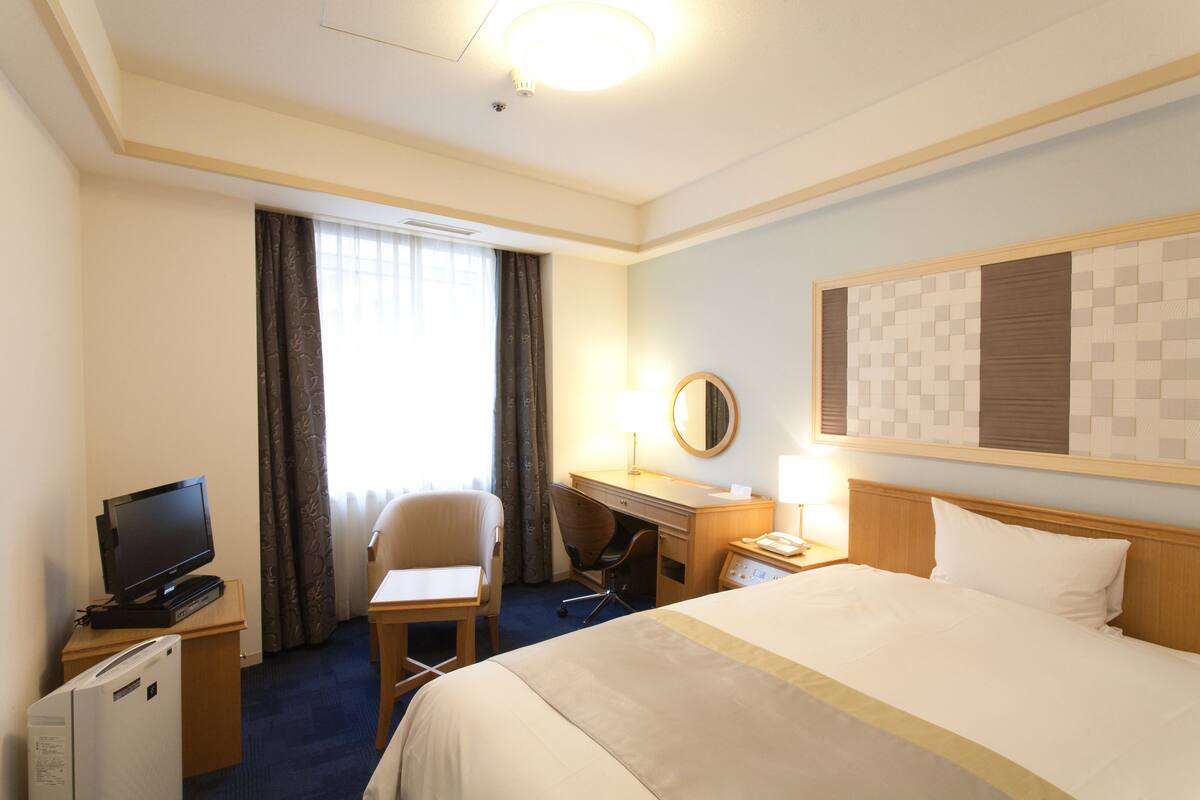 A hotel room with a bed, a desk, a chair, a television, and a refrigerator.
