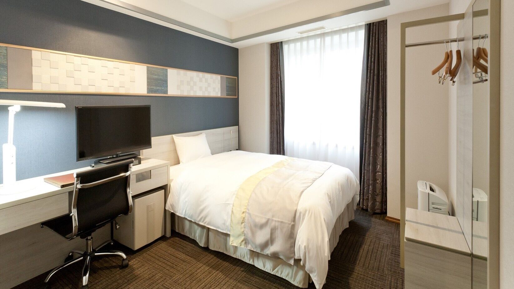 Une chambre d’hôtel équipée d’un lit, d’un bureau, d’une chaise, d’une télévision et d’une armoire.