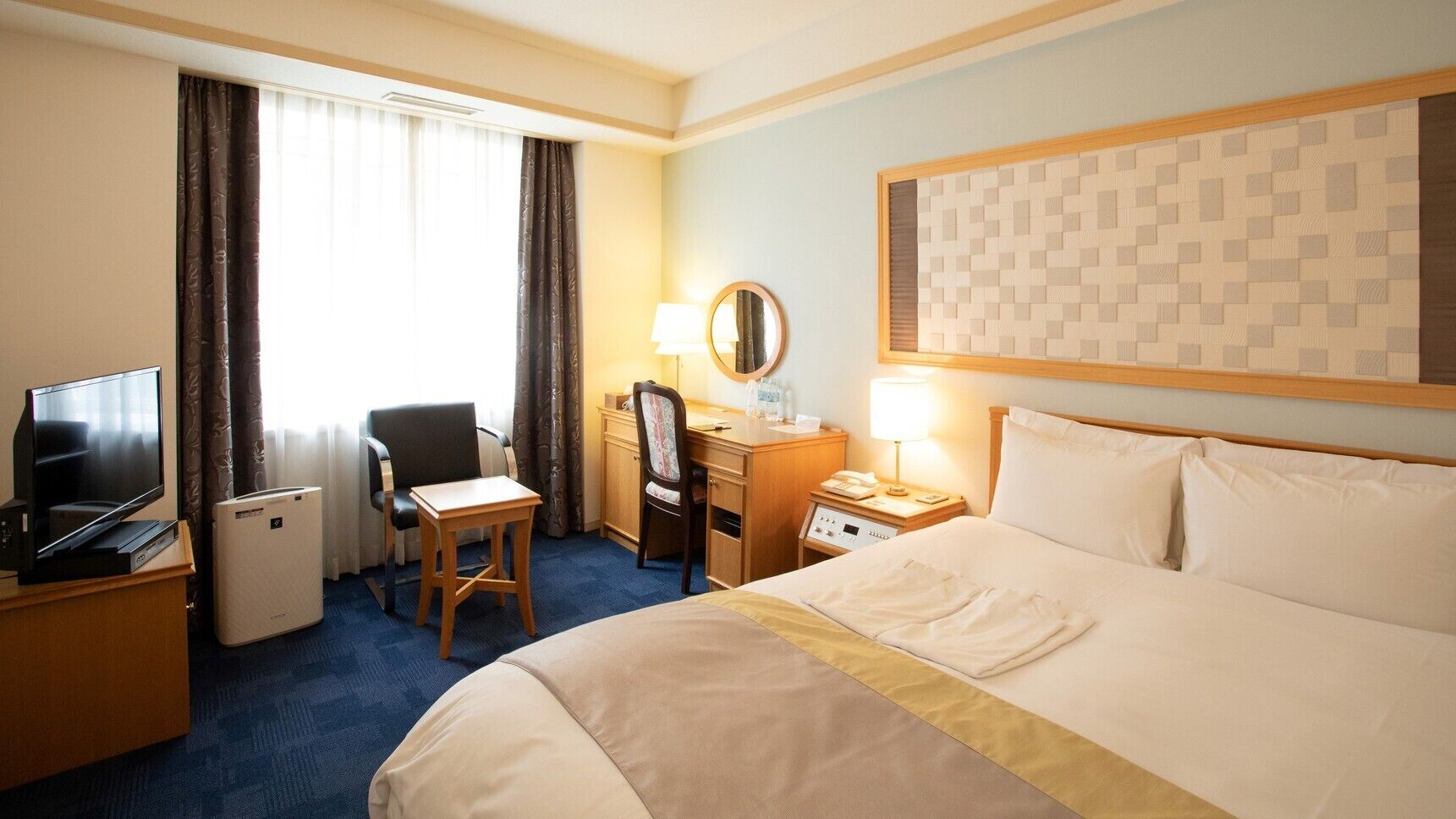 Une chambre d’hôtel équipée d’un lit, d’un bureau, d’une chaise, d’une télévision, d’une lampe et d’un miroir.