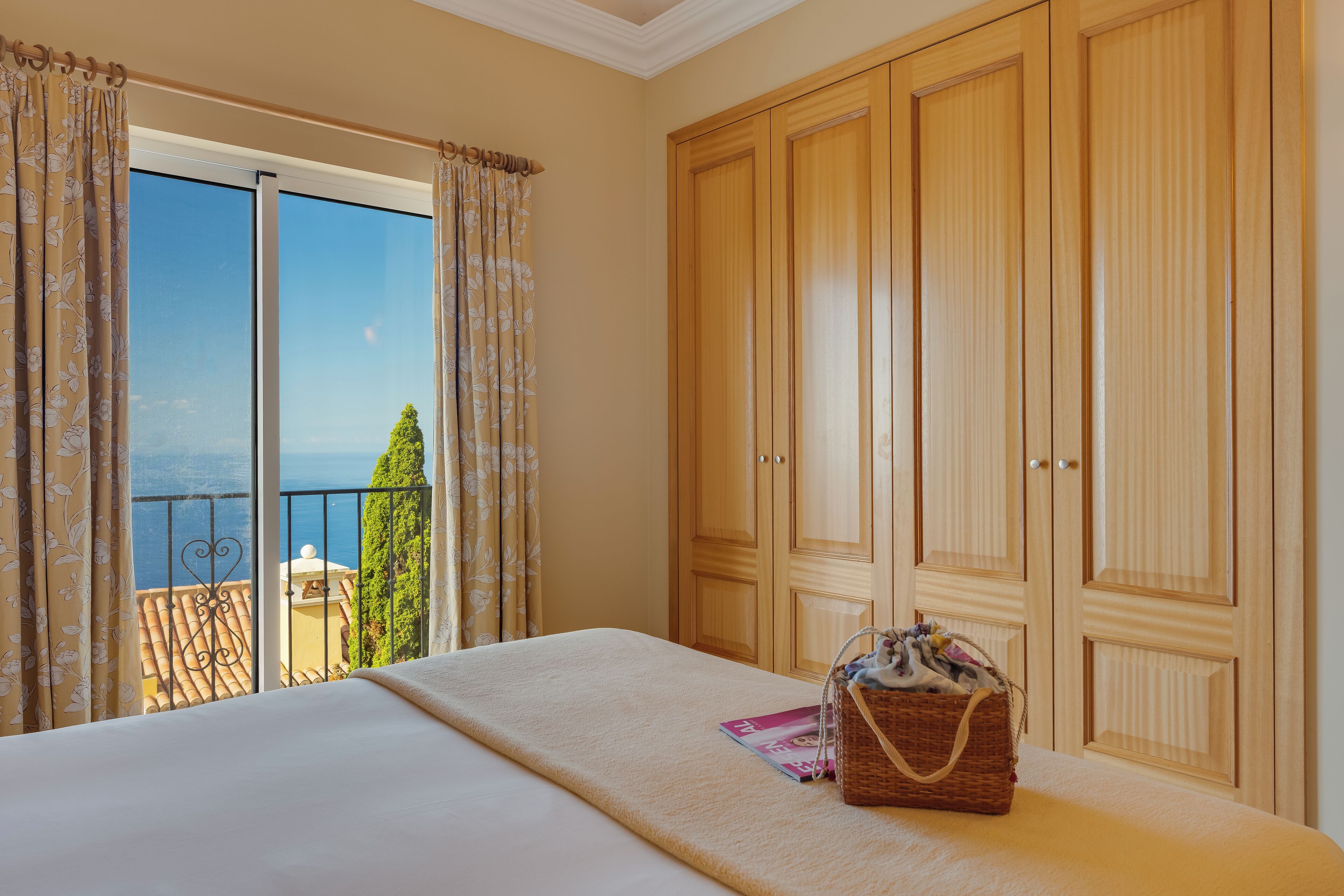 A bedroom with a bed, a wooden wardrobe, and a balcony with a view.