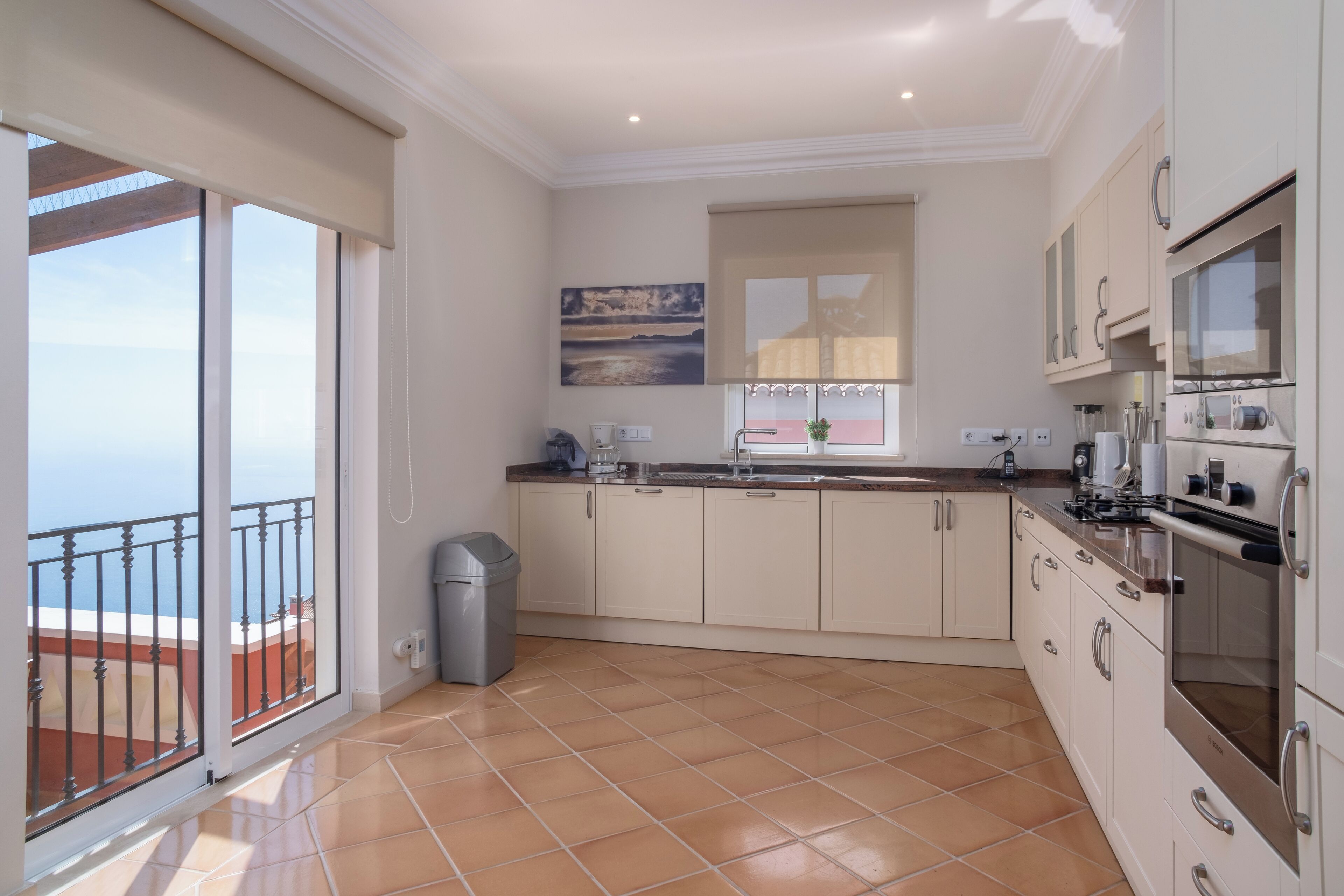 A modern kitchen with a large window, a balcony, and a view of the sea.