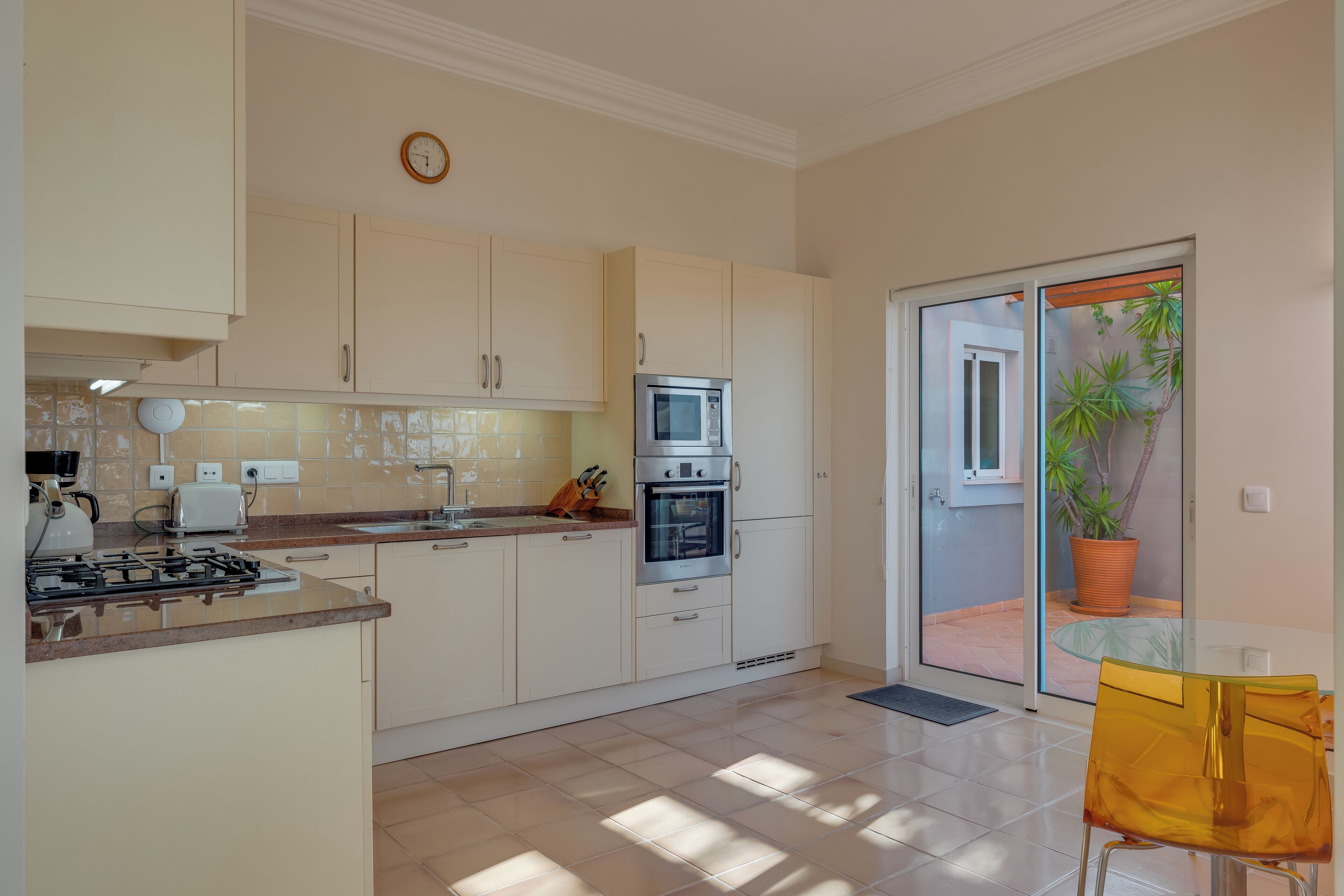 Een moderne keuken met witte kastjes, een fornuis, een magnetron en een broodrooster. Er is een glazen deur die leidt naar een balkon met een plant in een pot.