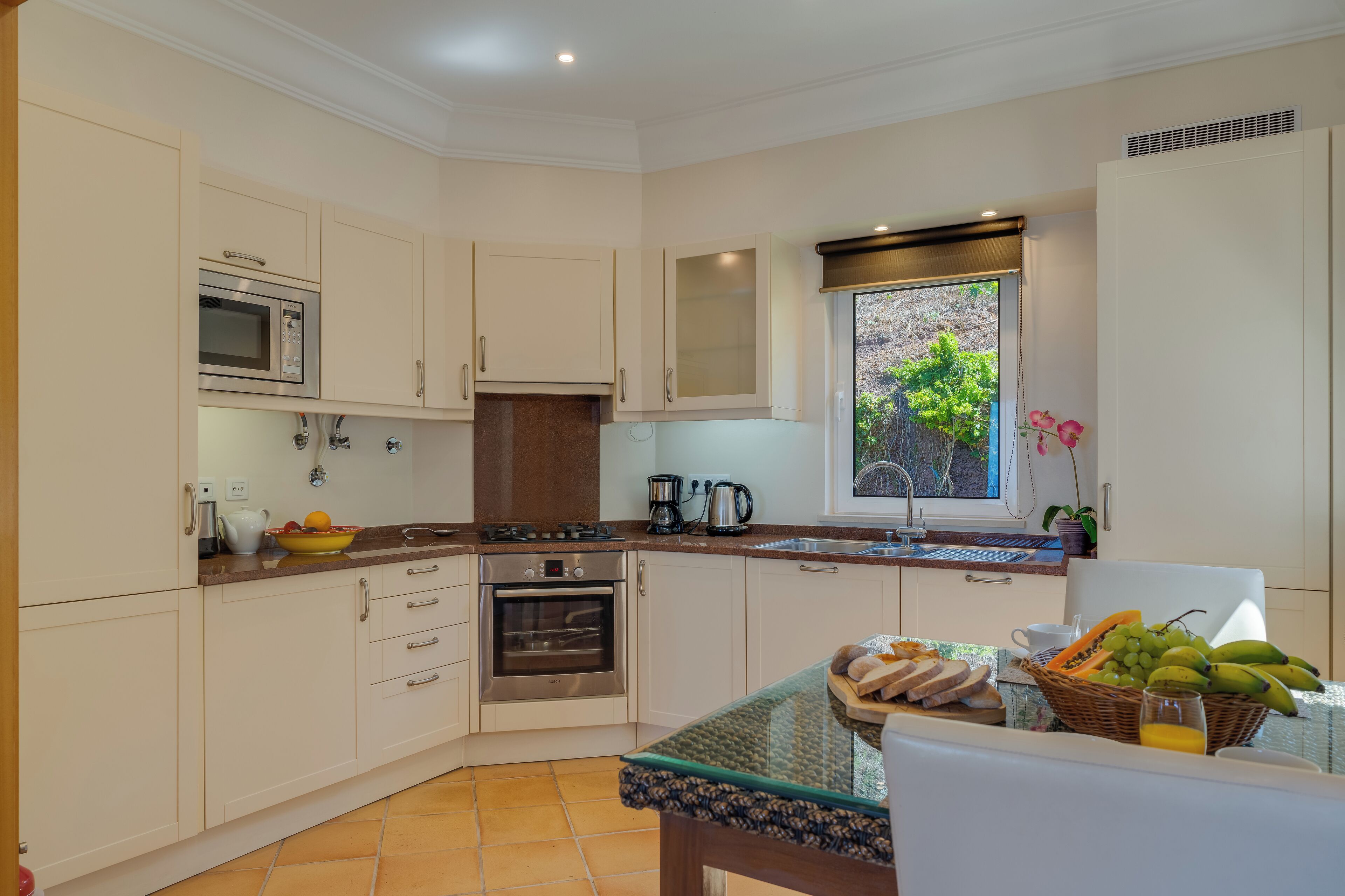 A modern kitchen with white cabinets, a built-in oven, a microwave, and a window with a view of greenery.