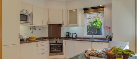A modern kitchen with white cabinets, a built-in oven, a microwave, and a window with a view of greenery.