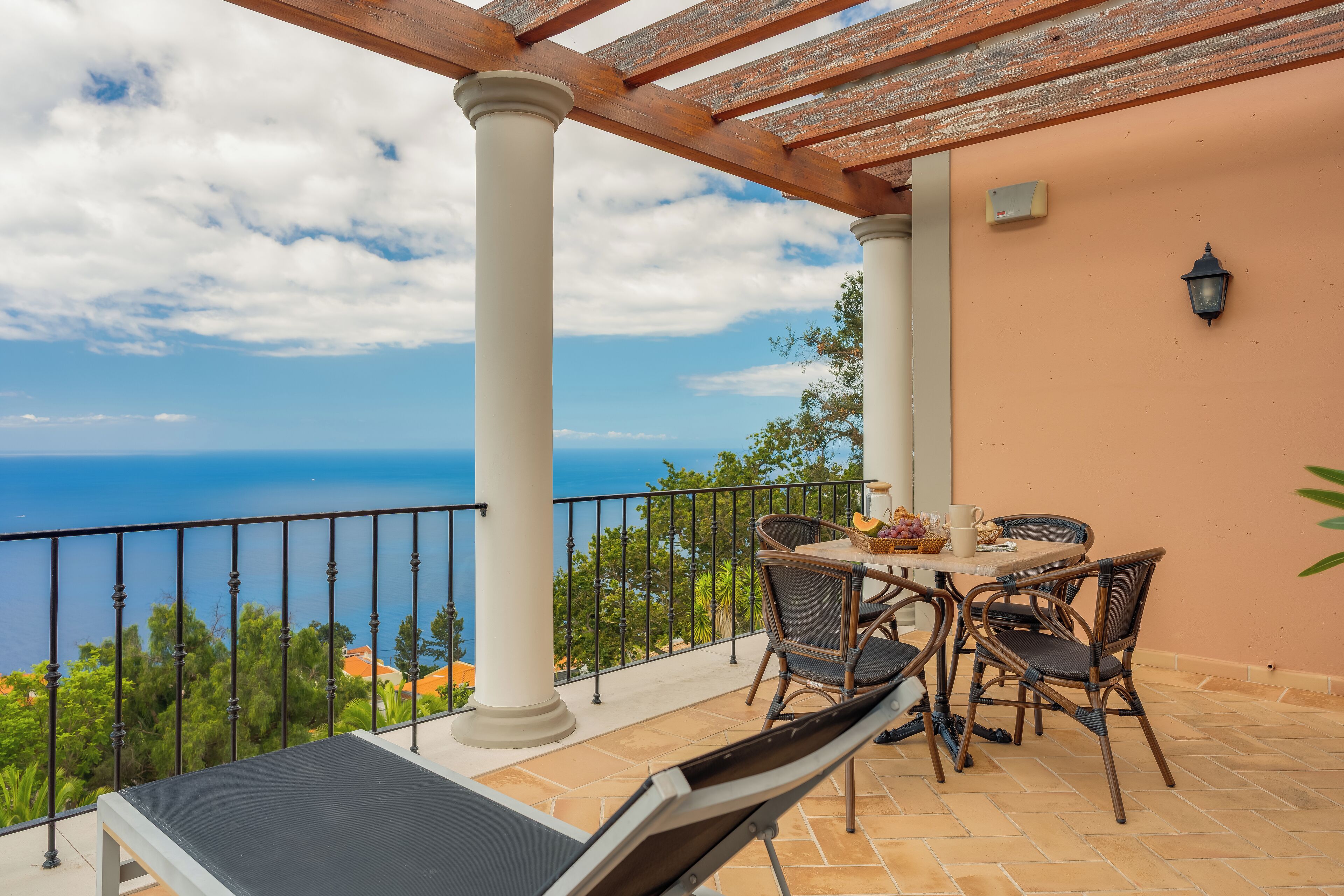 A balcony with a table and chairs, overlooking a scenic view of the sea.