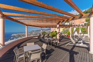 A rooftop terrace with wooden pergola, tables, chairs, and lounge chairs. - Palheiro Village (Funchal)