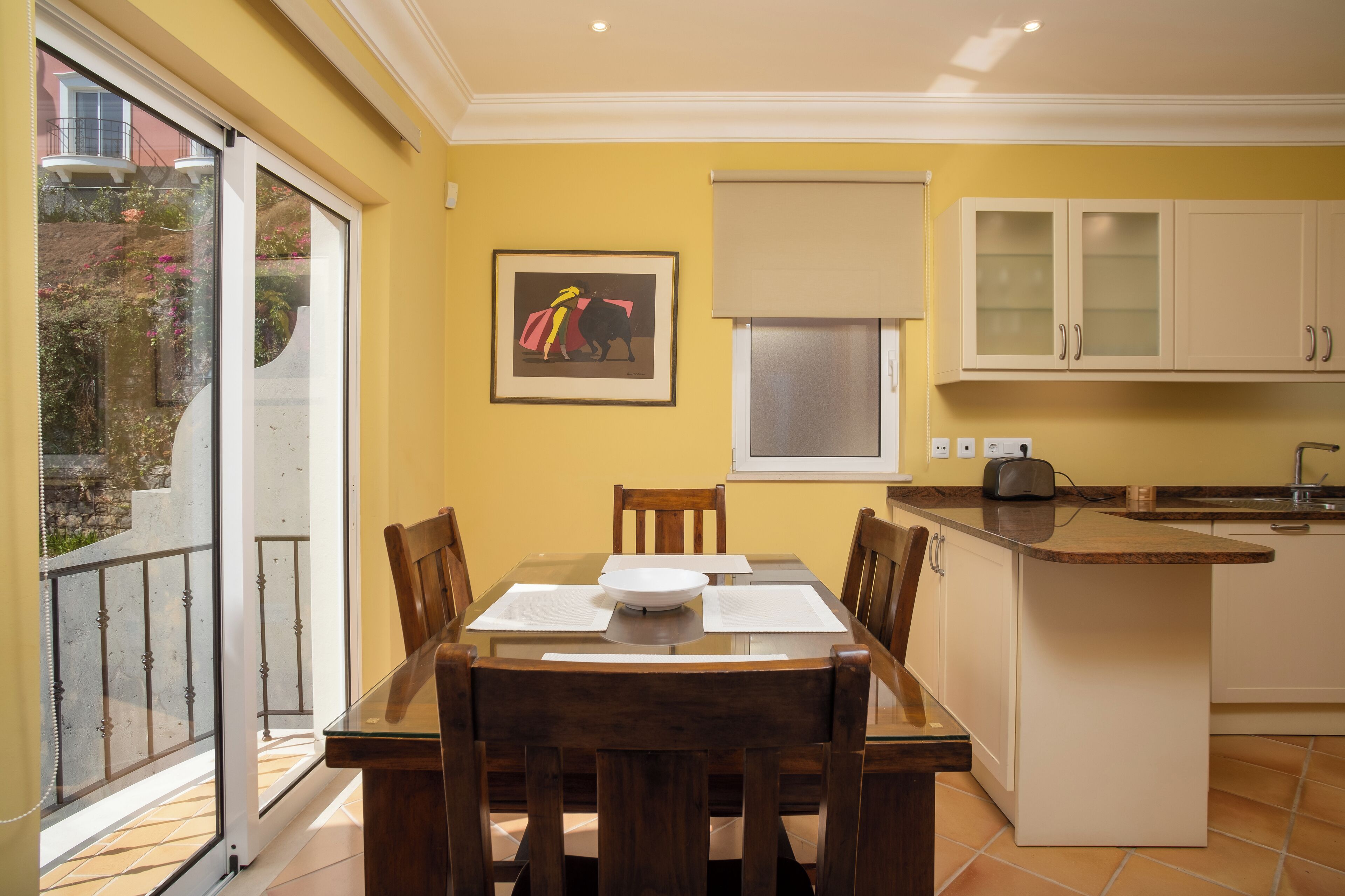 A dining area with a glass table, wooden chairs, and a kitchen with white cabinets.