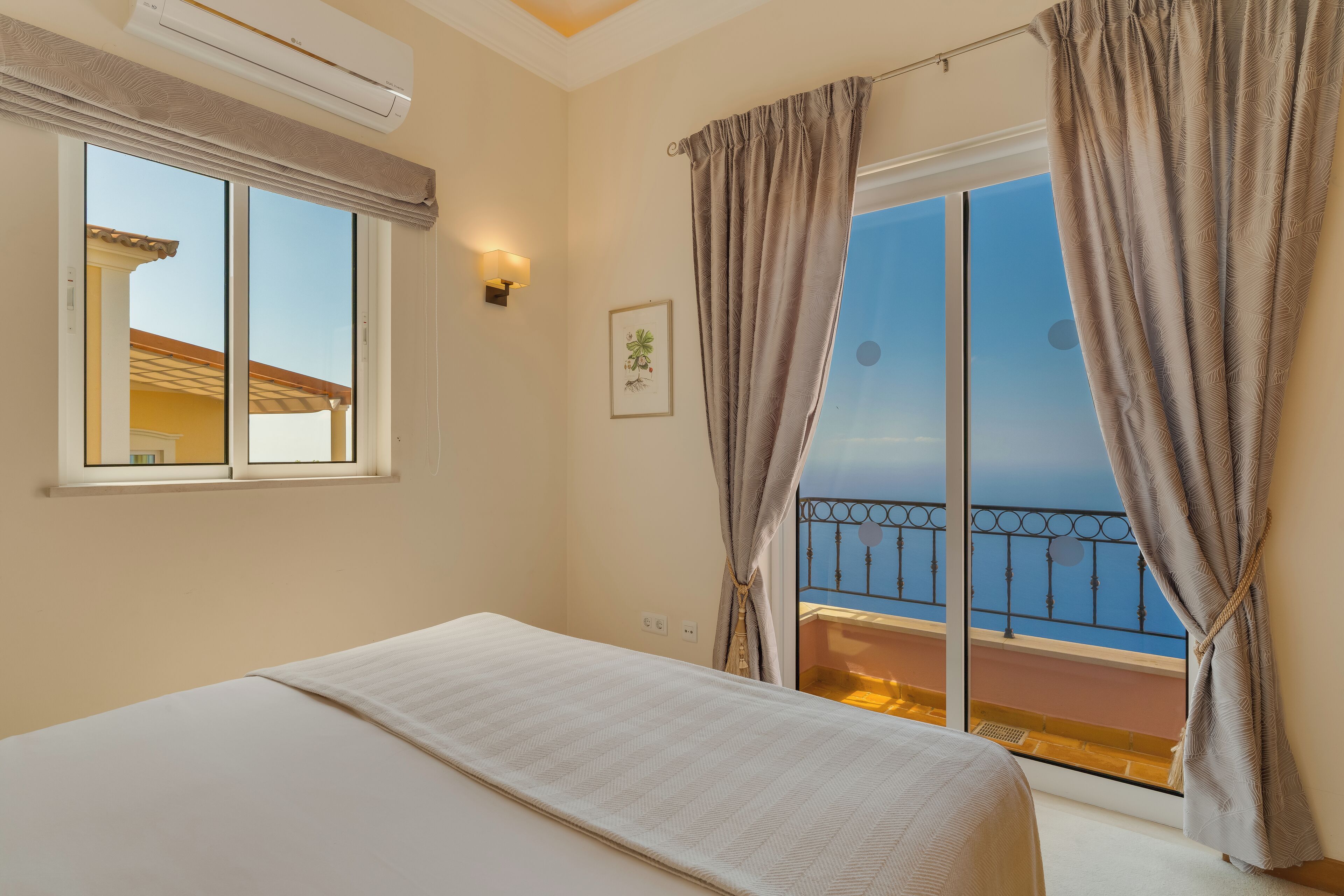 Una camera d'albergo con un letto, una finestra con tende, un condizionatore, una lampada a parete e un balcone con ringhiera.