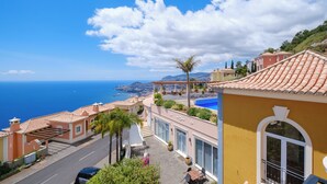 A coastal residential area with terracotta-roofed houses, a clear blue sky, and a view of the sea.
