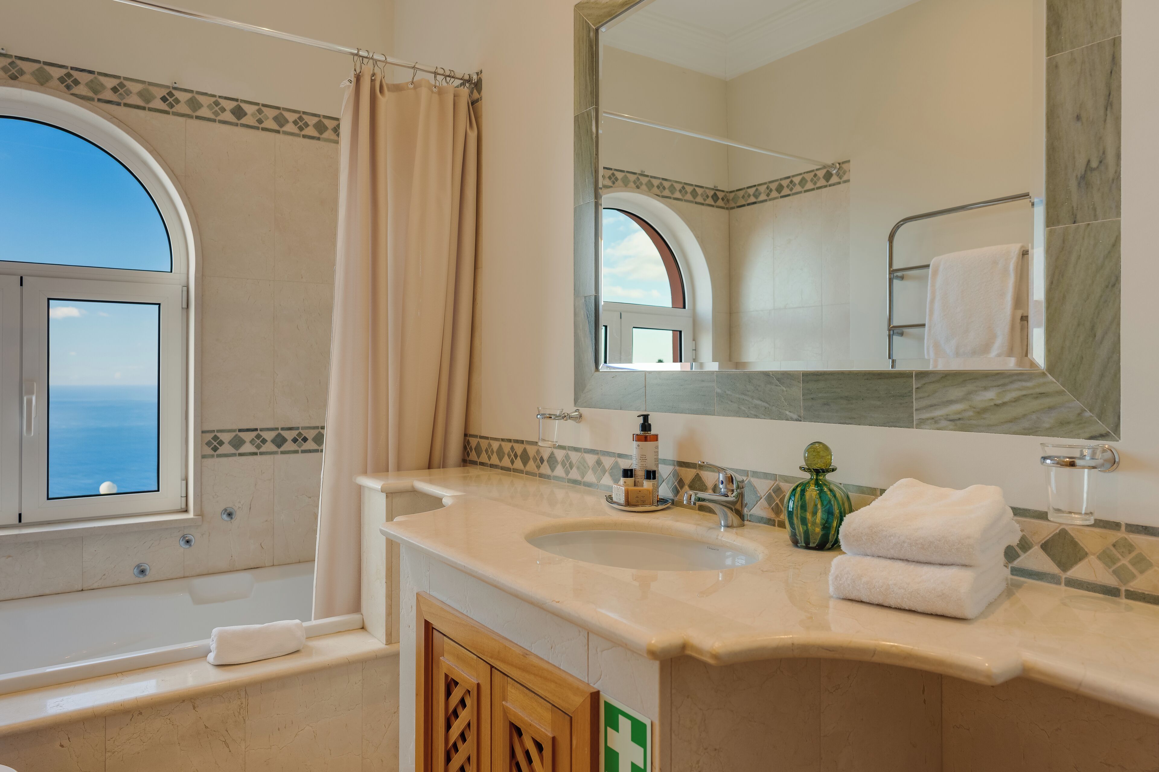 Un baño con bañera, lavamanos, espejo y ventana con vista al mar.