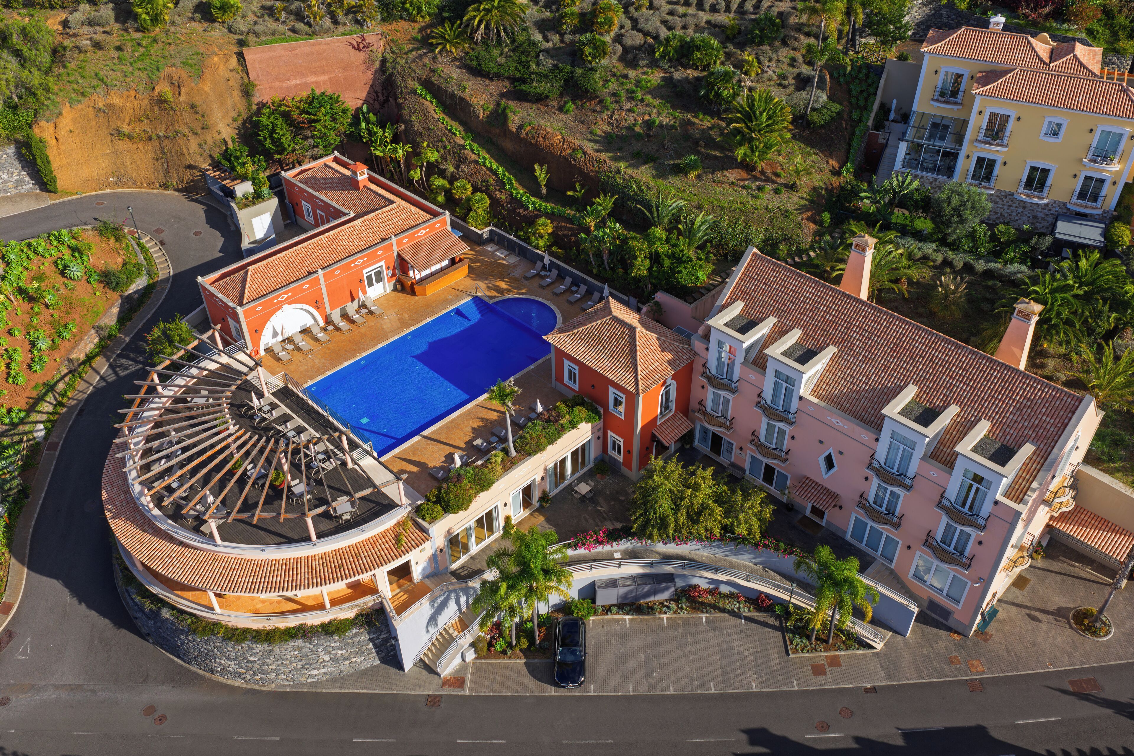 An aerial view of a residential property with a swimming pool, curved driveway, and multiple buildings with balconies.