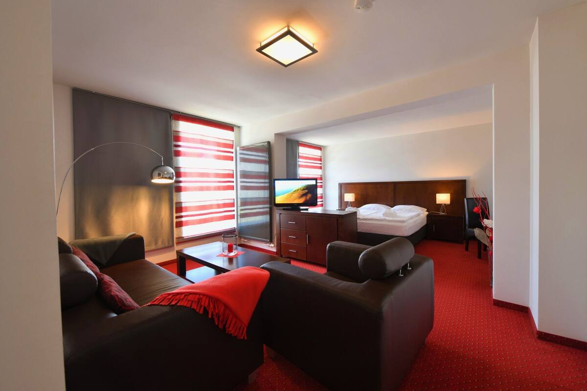 A modern hotel room with a sofa, a TV, a bed, and a red carpet.