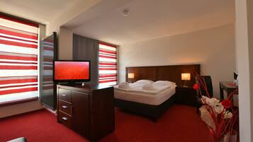 Una habitación de hotel con una cama, un escritorio con televisor, un aparador, una mesita de noche con lámparas y un florero con flores.