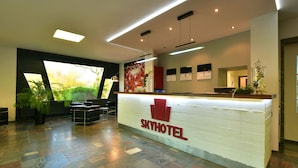 A reception desk with a logo, a large window, and a plant. - SKYHOTEL Merseburg (Merseburg)
