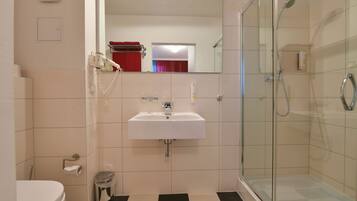 A bathroom with a white sink, a glass shower enclosure, and a checkered floor.