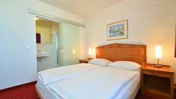 Ein Hotelzimmer mit einem großen Bett, zwei Nachttischen mit Lampen, einem Gemälde an der Wand und einem durchgegangenen Tür erkennbaren Badezimmer.