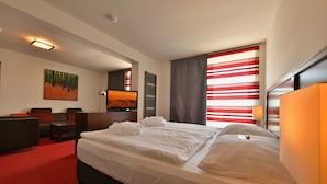 A hotel room with a large bed, a sofa, a desk, and a painting on the wall. - SKYHOTEL Merseburg (Merseburg)