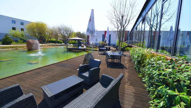 An outdoor patio with a pool, seating, and a view of a modern building. - SKYHOTEL Merseburg (Merseburg)