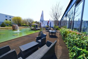 An outdoor patio with a pool, seating, and a view of a modern building. - SKYHOTEL Merseburg (Merseburg)