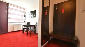 A hotel room with a red carpet, a wooden bench, a table with chairs, a radiator, and a wall-mounted picture.