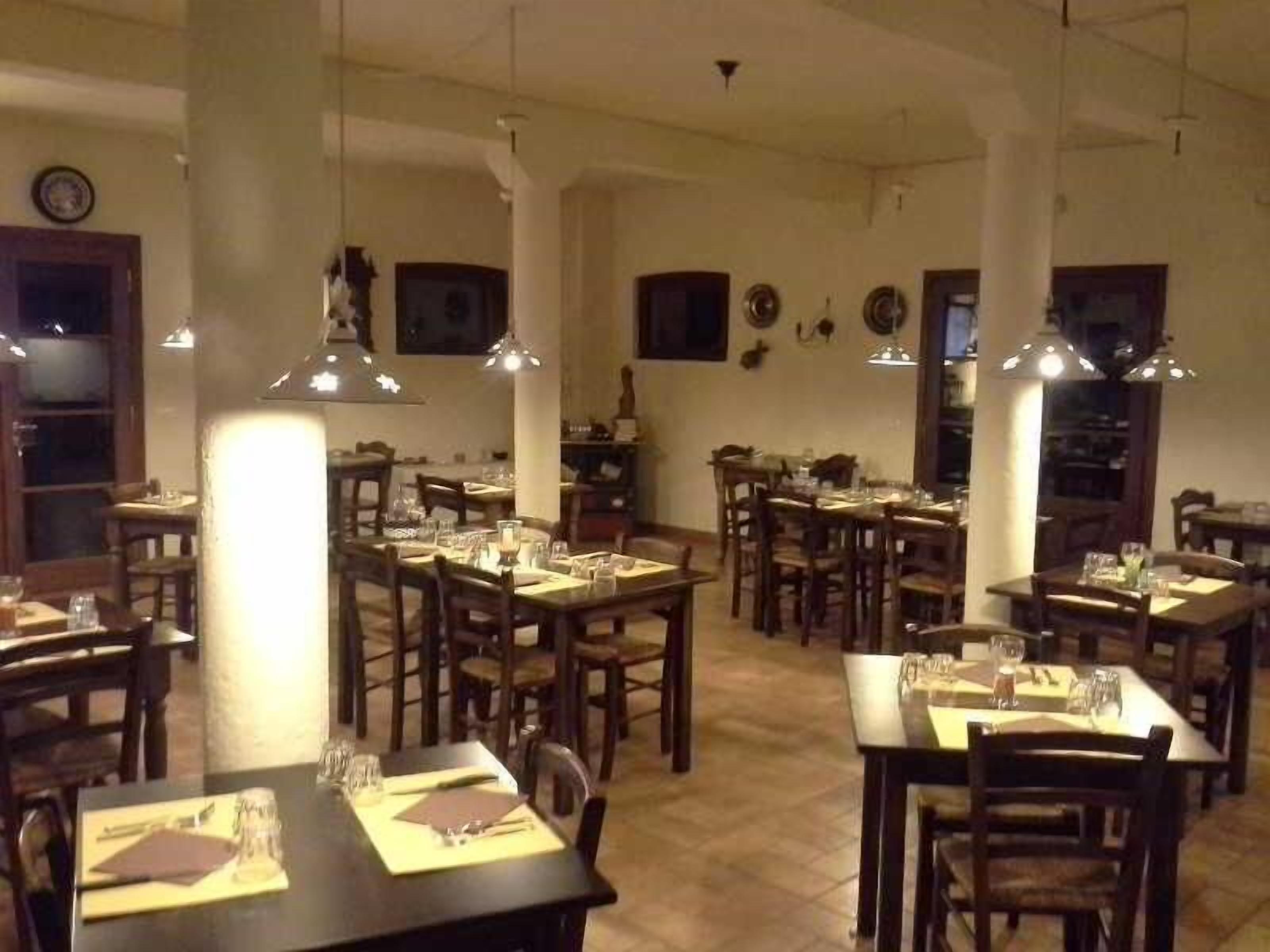 Un restaurante con varias mesas y sillas, piso de madera e iluminación colgante.