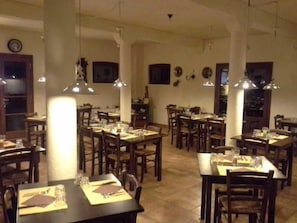 Un restaurante con varias mesas y sillas, piso de madera e iluminación colgante.