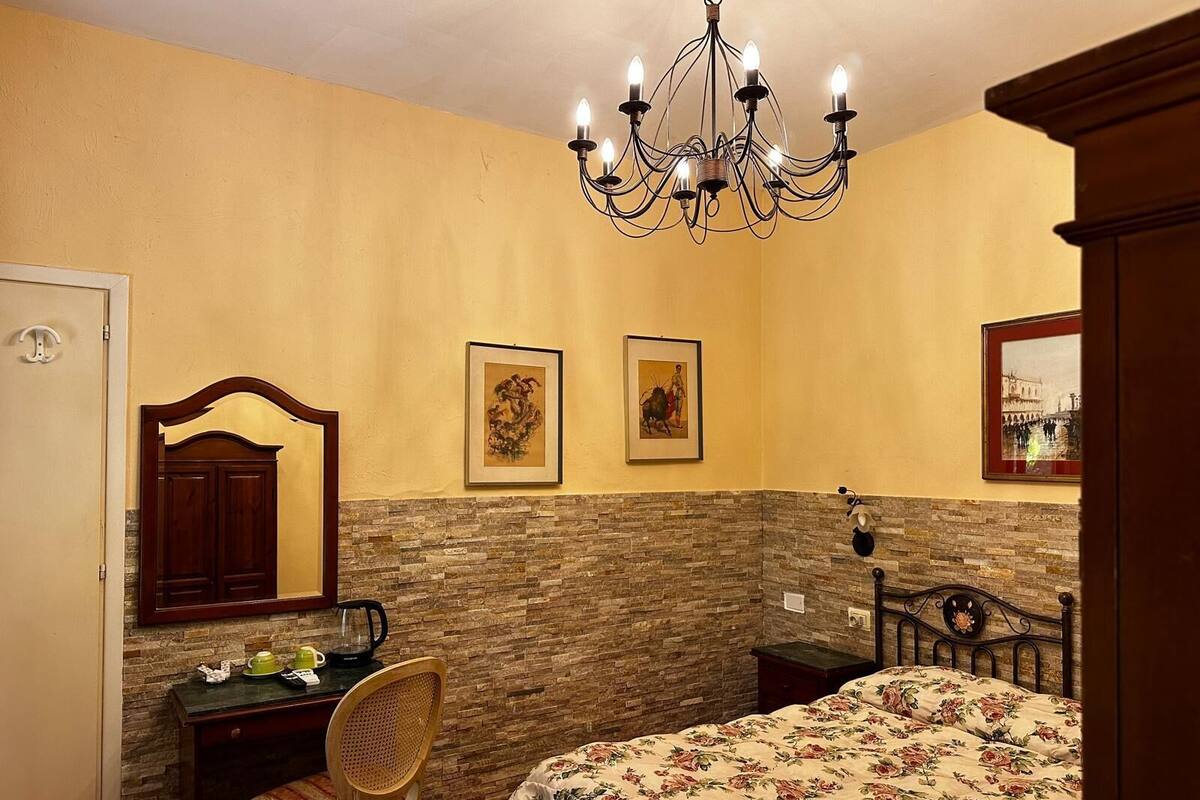 Un dormitorio con cama, escritorio, silla, candelabro y dos cuadros en la pared.