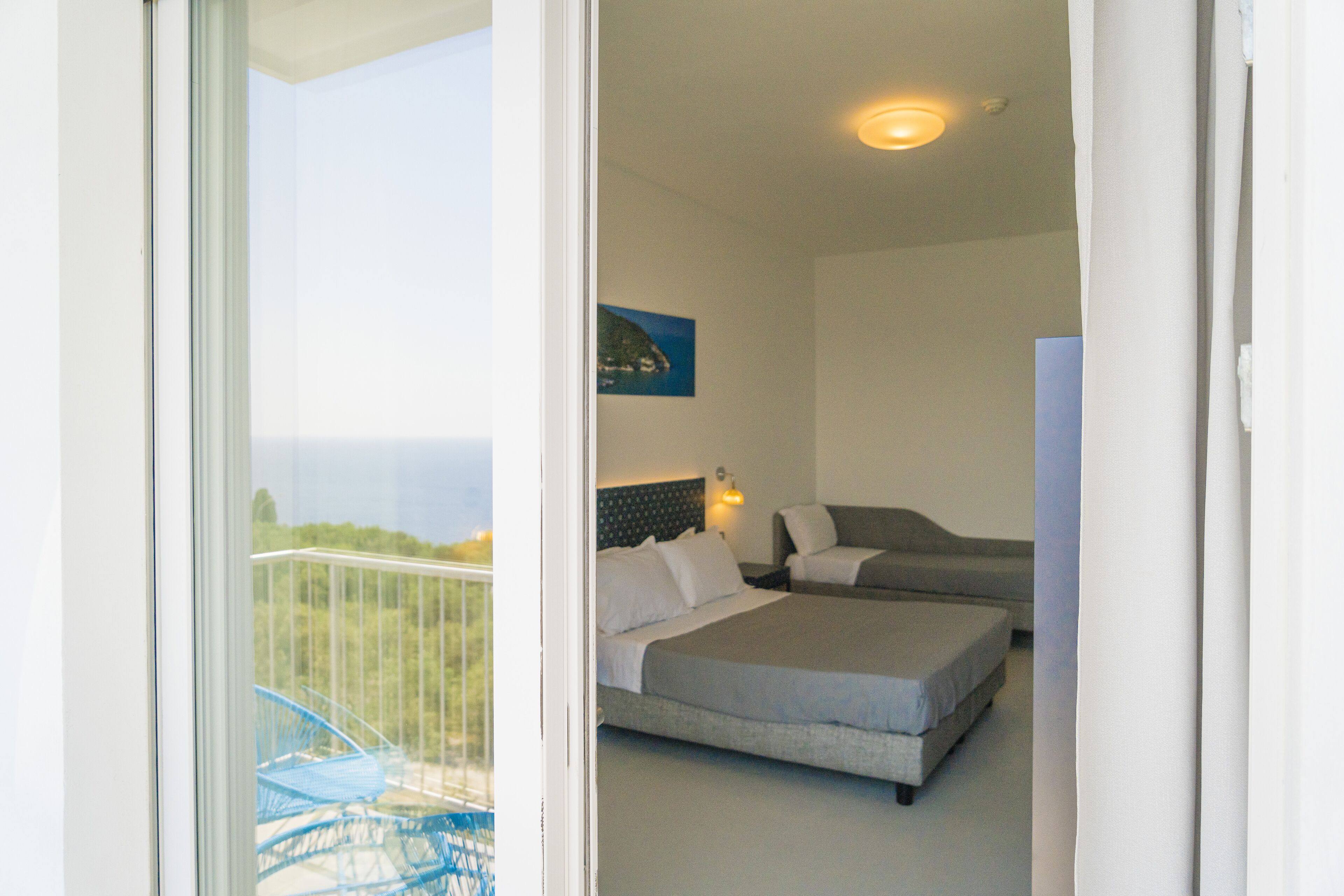 A hotel room with two beds, a balcony with a chair, and a painting on the wall.
