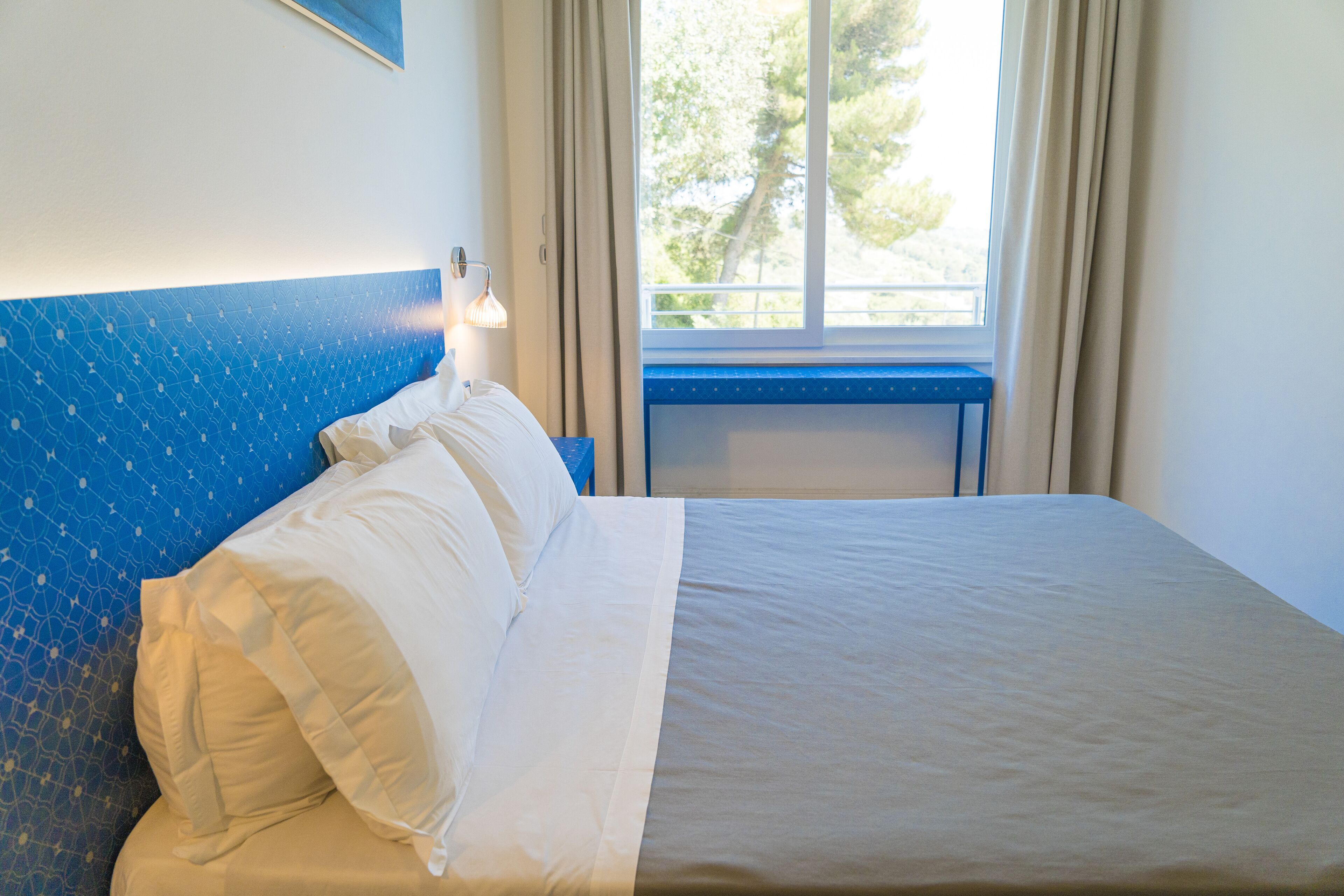 Une chambre d’hôtel avec un lit, une table de chevet, une lampe et une fenêtre avec des rideaux.