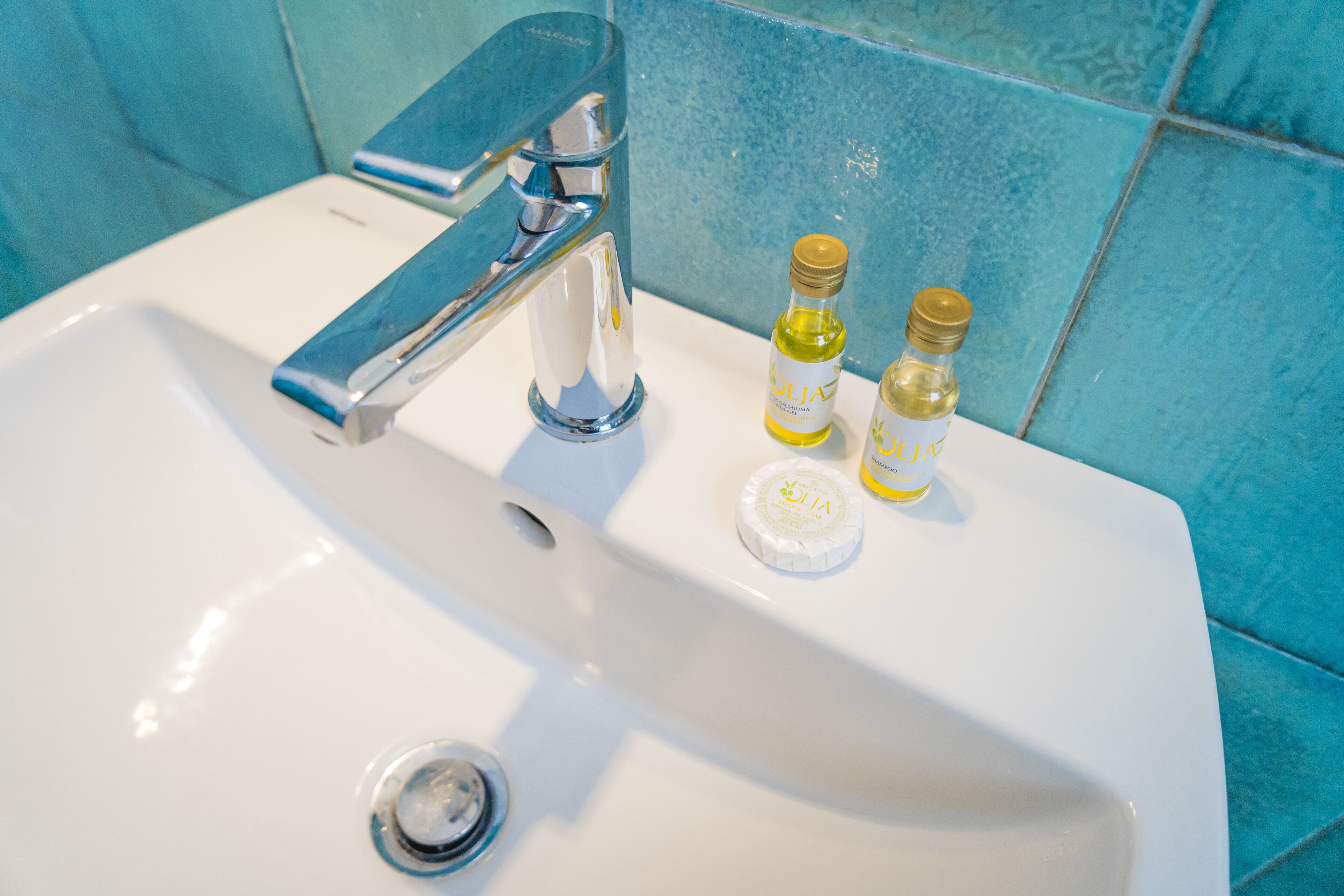 Ein weißes Waschbecken mit Chromarmatur, zwei kleine Flaschen mit Flüssigkeit und eine Seifenschale.