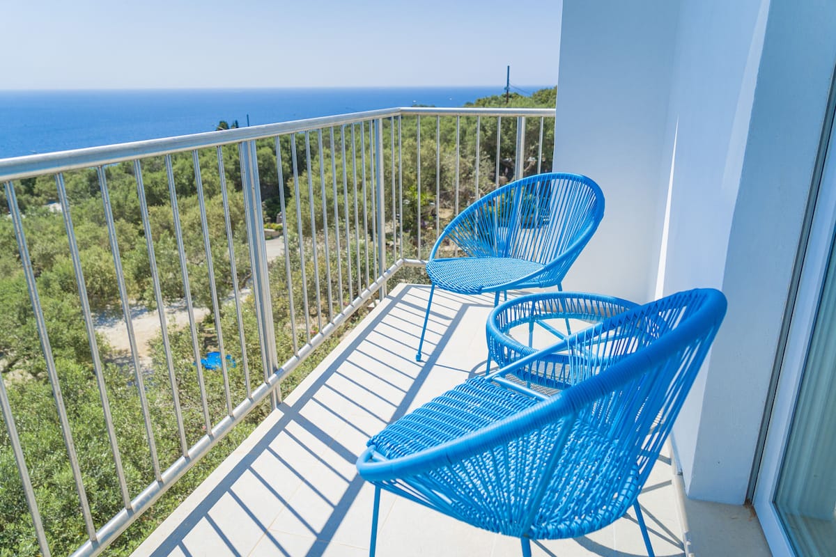 A balcony with two blue chairs and a view of the ocean.