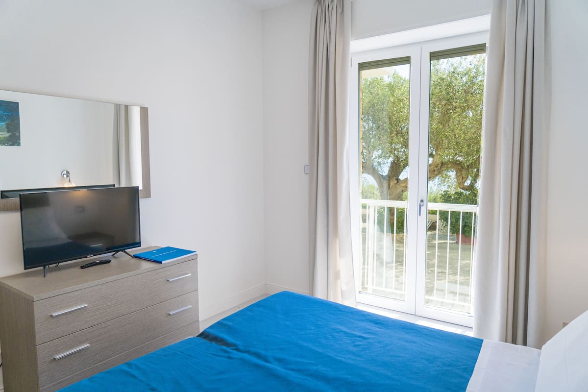 A bedroom with a bed, a TV on a dresser, and a sliding glass door to the outside.