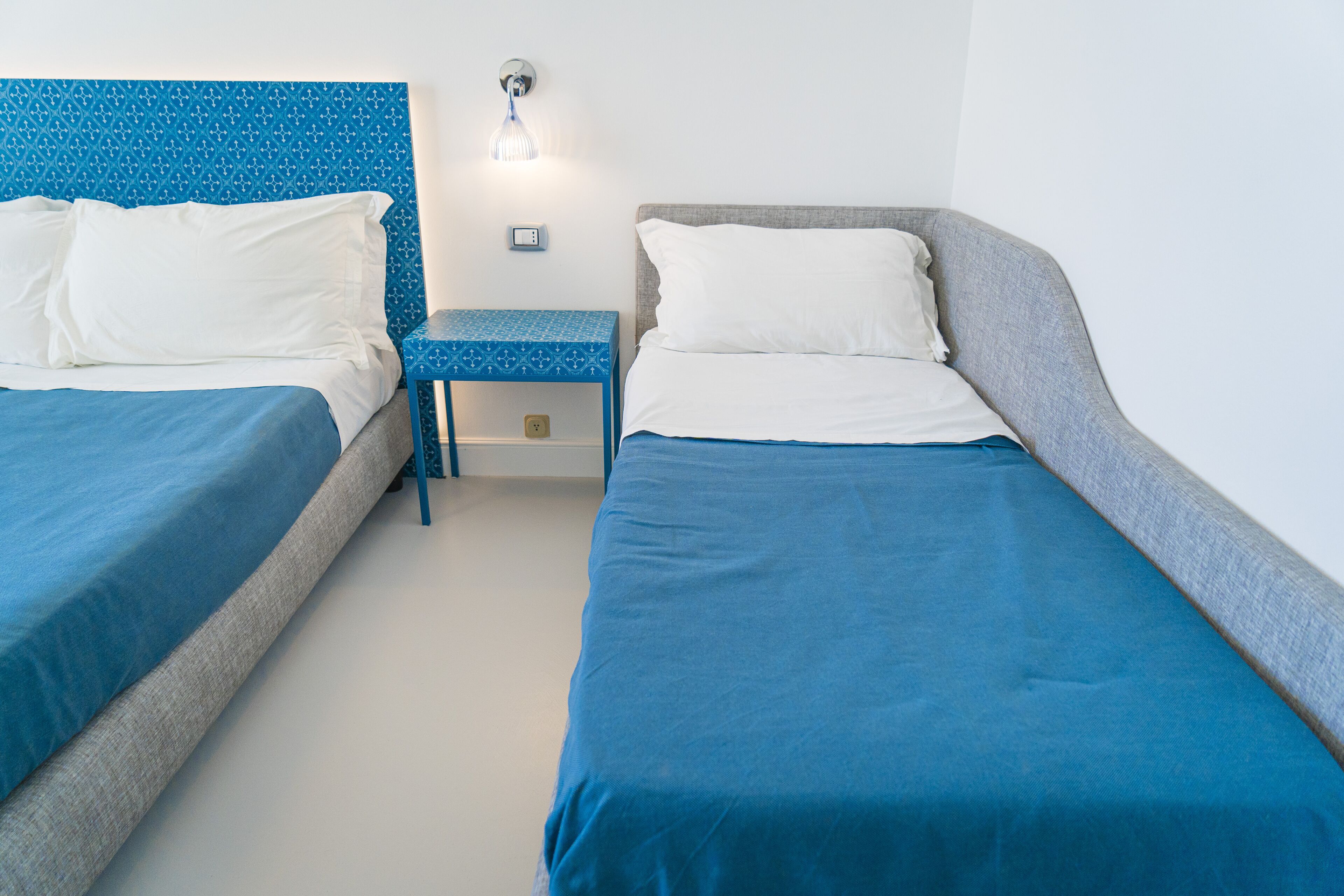 A twin room with two beds, a small table, and a wall-mounted light fixture.