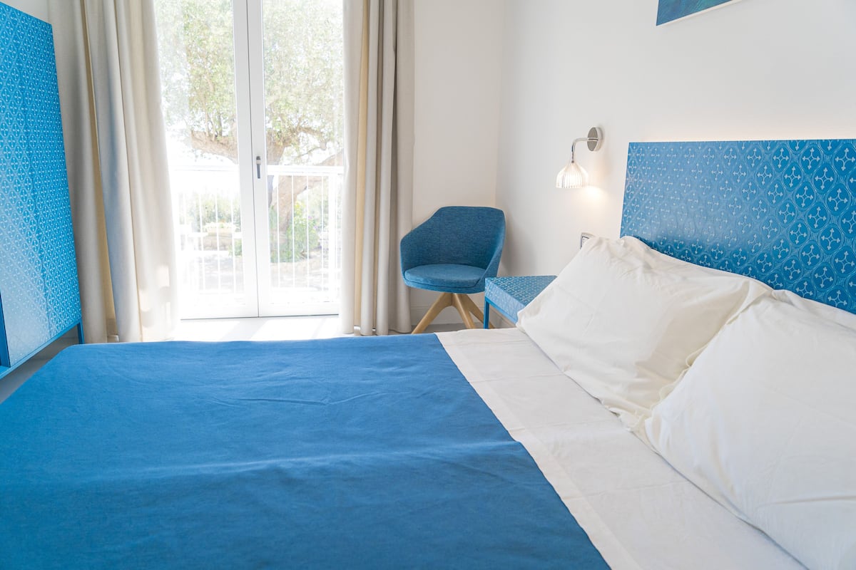 A hotel room with a large bed, a chair, and a view of the outdoors through a glass door.