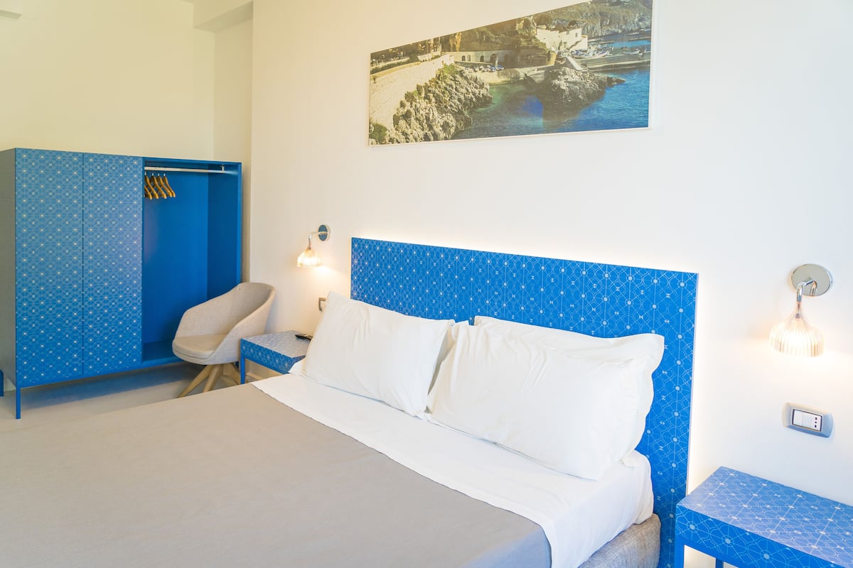 A bedroom with a bed, a chair, a wardrobe, and a wall-mounted light fixture.