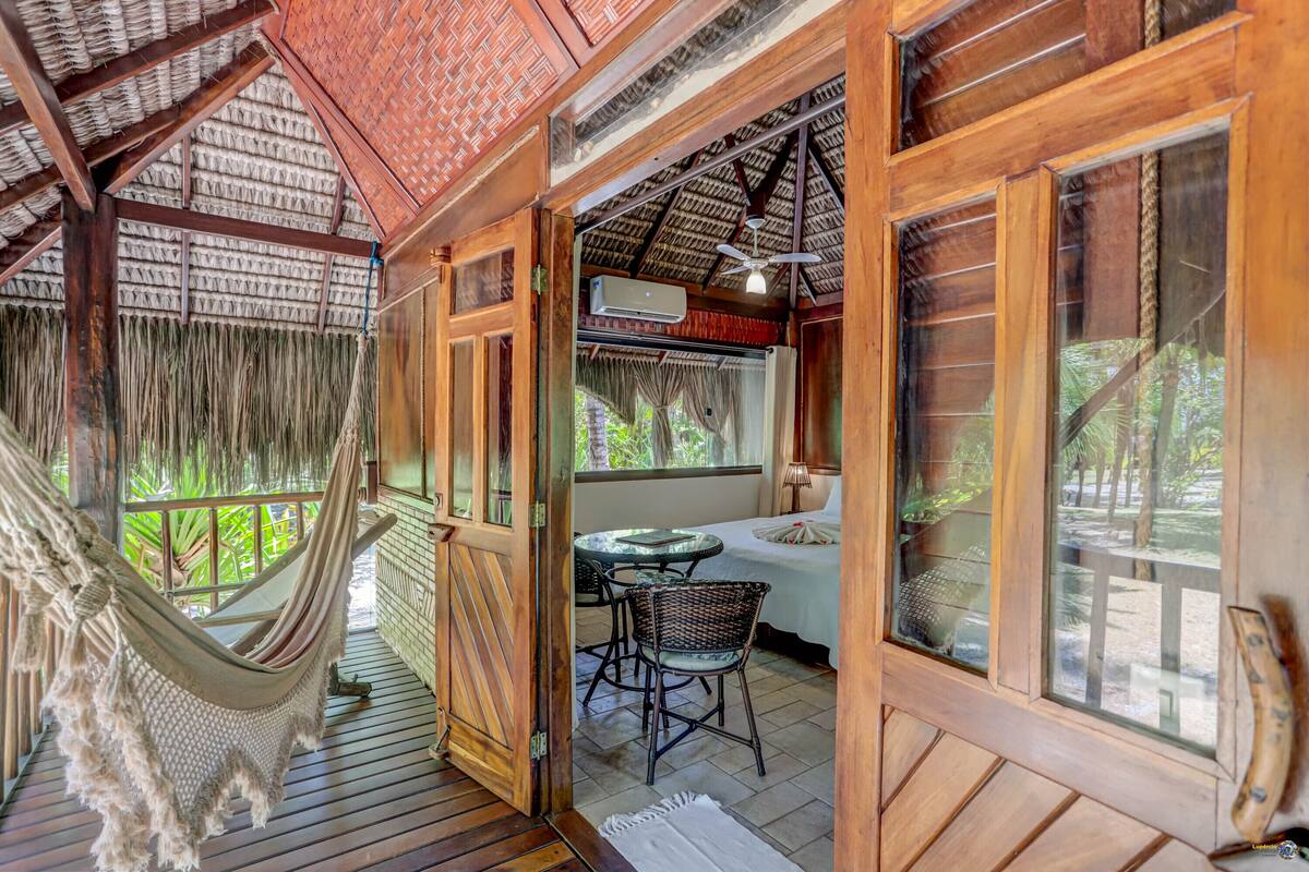 A wooden room with a hammock, a table with chairs, and a bed.