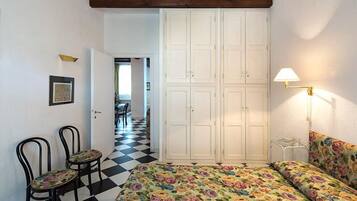 A bedroom with a checkered floor, a bed with floral bedding, two chairs, a wardrobe, and a lamp.