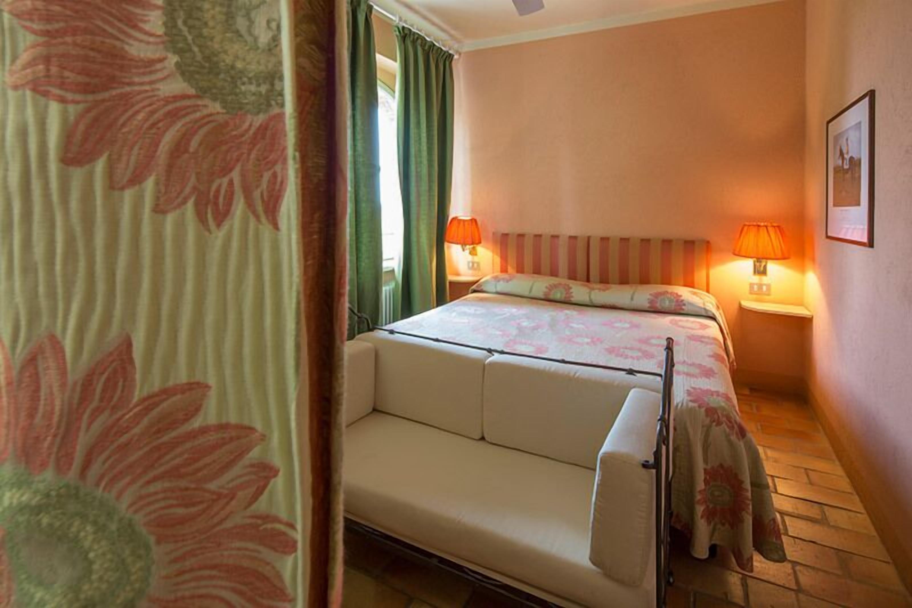 Een hotelkamer met een bed, een slaapbank, twee bedlampen en een ingelijst schilderij aan de muur.