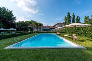 A rectangular swimming pool with a metal ladder, surrounded by well-manicured grass and trees.