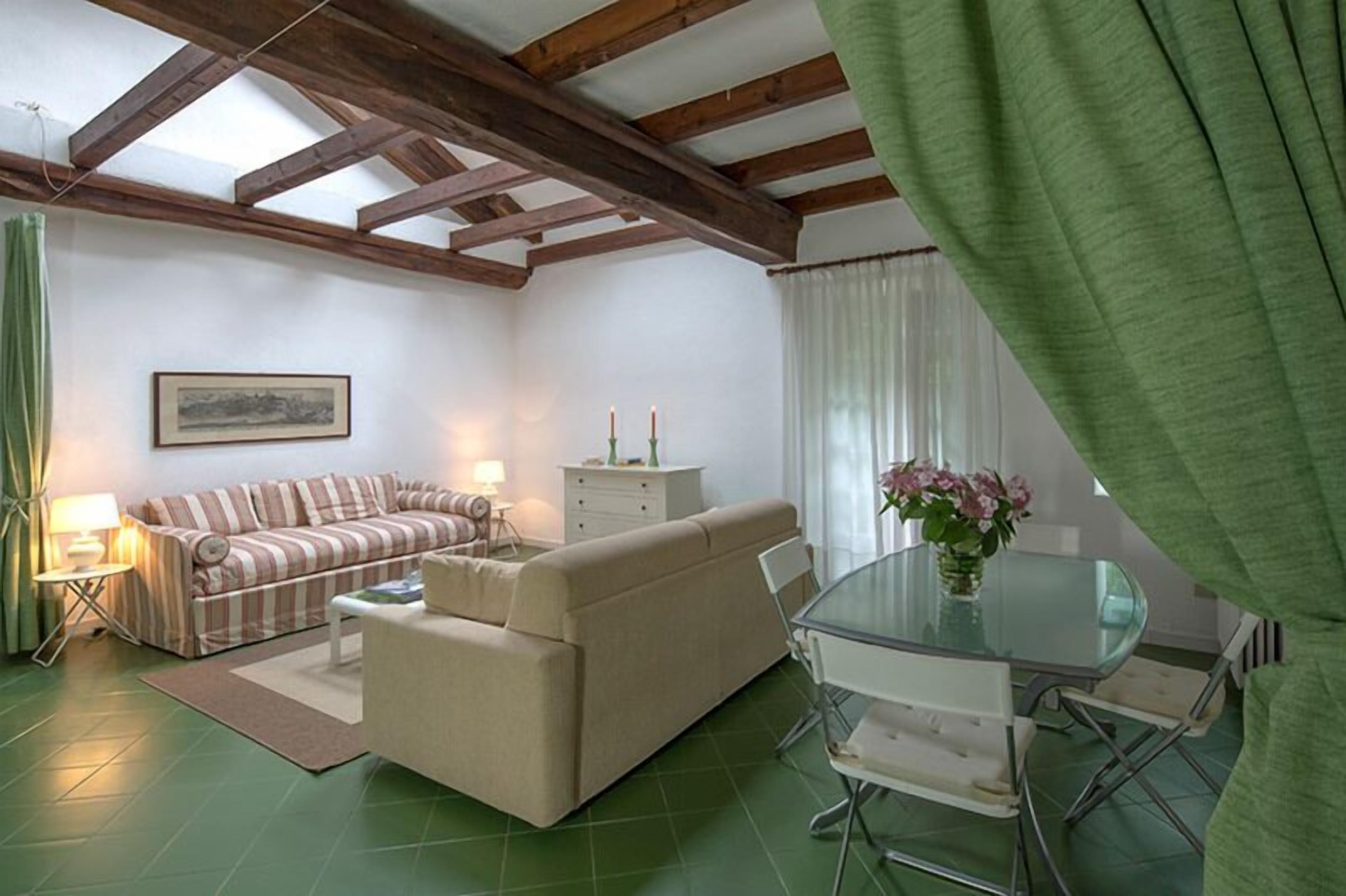 A living room with a striped sofa, a beige sofa, a glass dining table, and a green curtain.