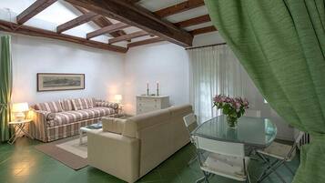 A living room with a striped sofa, a beige sofa, a glass dining table, and a green curtain.