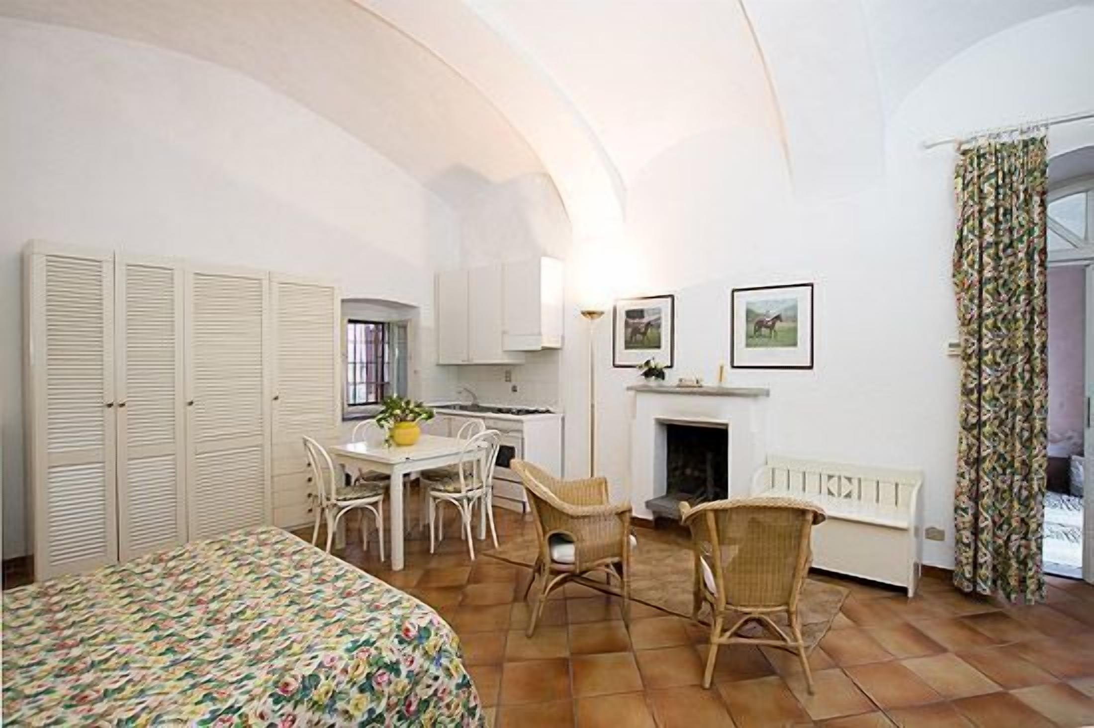 A room with a bed, a dining table with chairs, a fireplace, and a kitchen area.