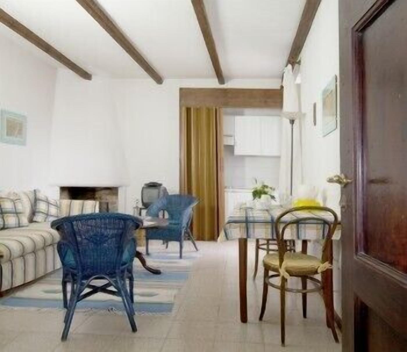 Ein Wohnzimmer mit einer Couch, zwei blauen Sesseln, einem Holzesstisch mit Stühlen und einer Küche im Hintergrund.